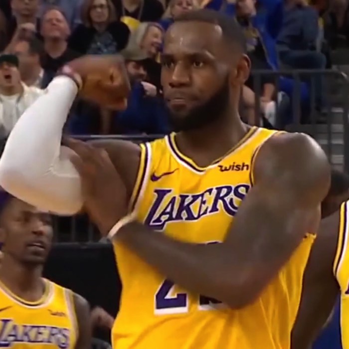 Basketball player in yellow jersey flexes arm on court, with spectators in the background.