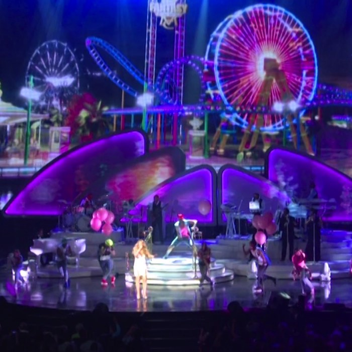 Concert stage with performers and colorful Ferris wheel and roller coaster visuals in the background.