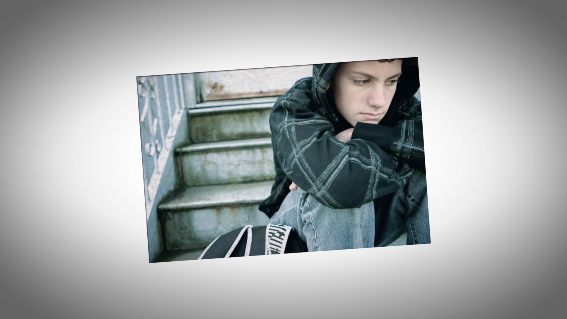 Person sitting on outdoor steps, wearing a hoodie, looking contemplative with arms crossed over knees.