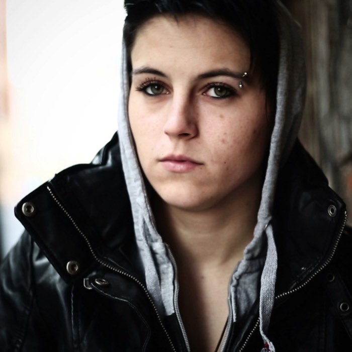Person wearing a dark jacket and hoodie, looking directly at the camera with a neutral expression.