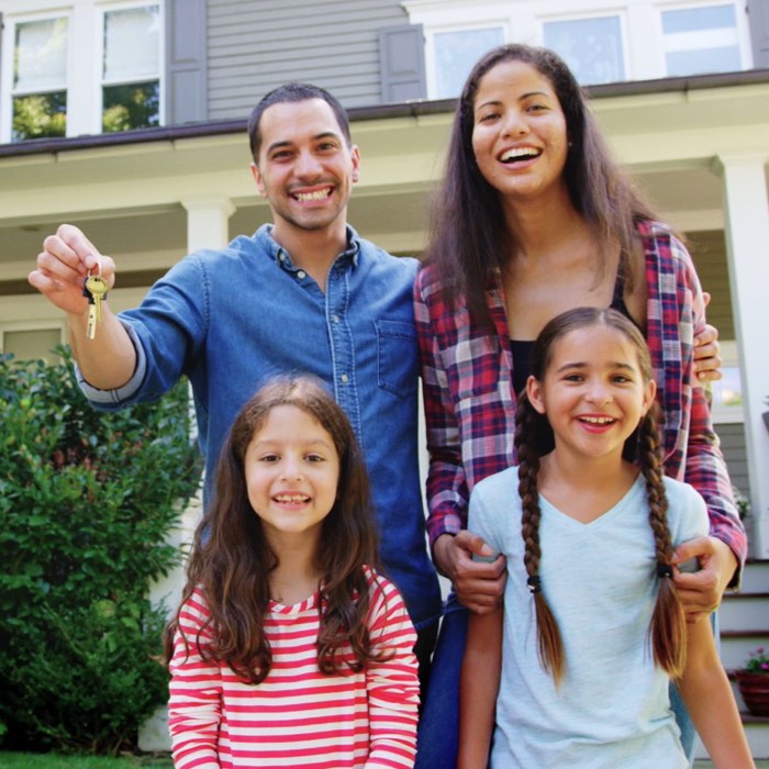 A smiling family of four holding a key, standing in front of their new house.