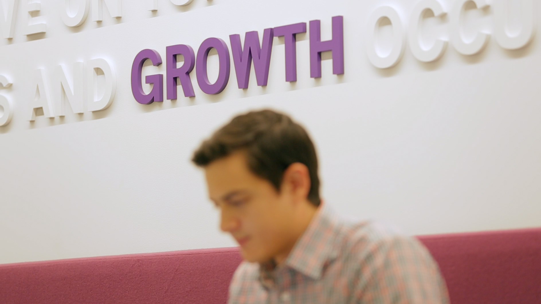 Blurred person in front of a wall with "GROWTH" in large purple letters.