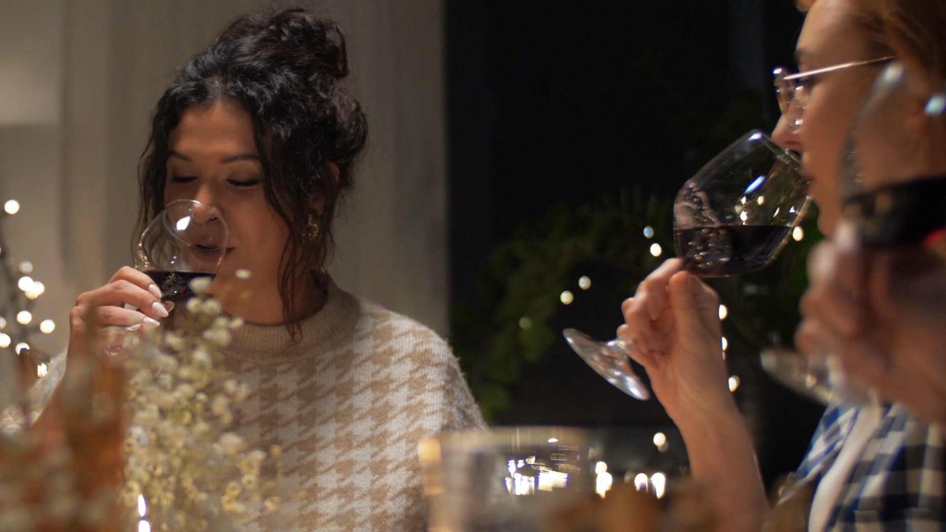 Two people enjoying glasses of wine at a candlelit table with soft lighting and visible decorative foliage.