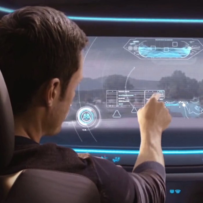 Person interacts with a futuristic touchscreen displaying maps and data inside a car.