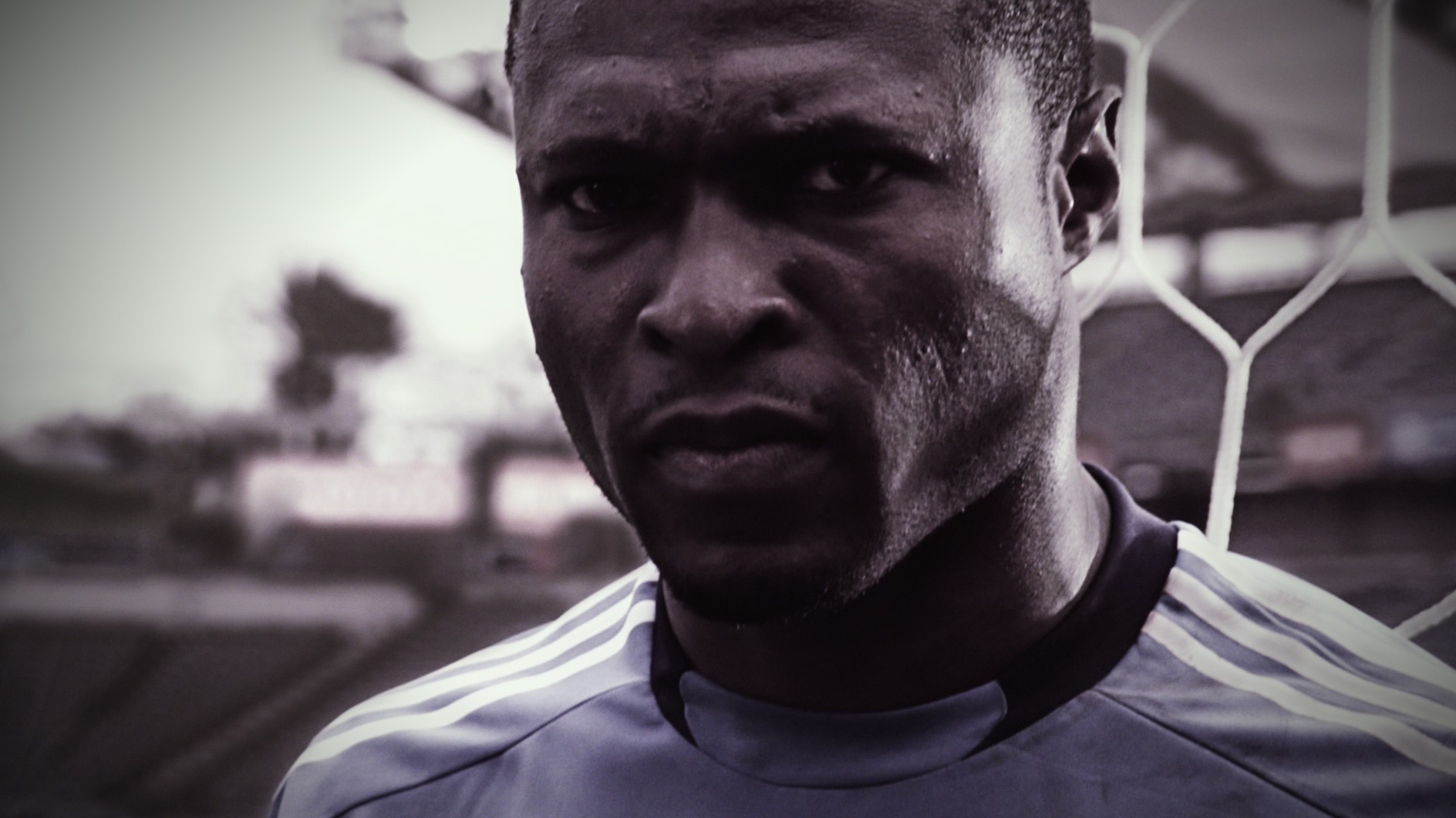 Close-up of a soccer player in a blue jersey, standing focused with a netted goal in the background.