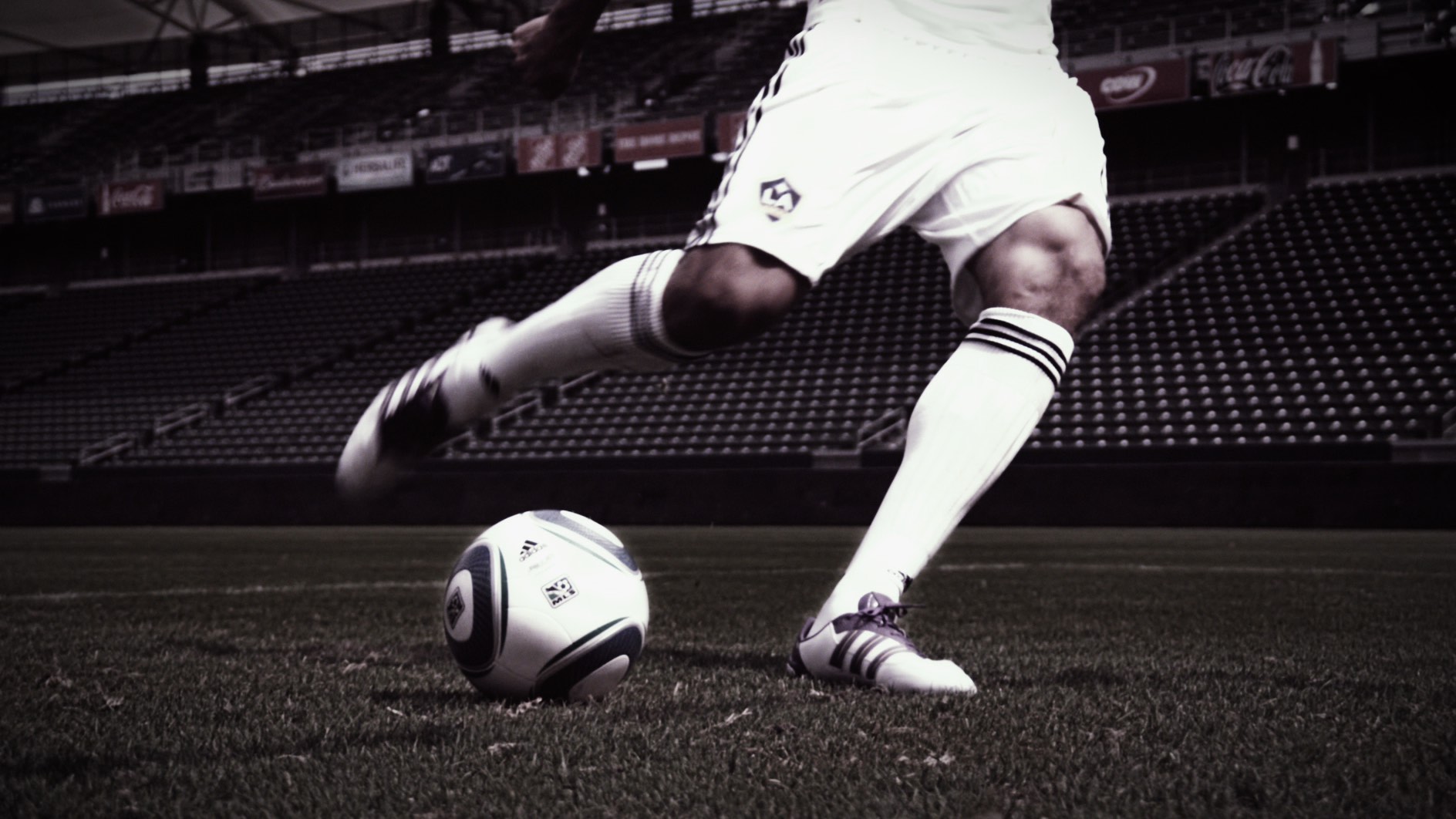 Soccer player in white strikes a ball on a grass field in a stadium, with mid-action motion blur.