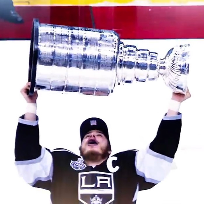 Hockey player in a black and white jersey lifts a large silver trophy triumphantly above his head.