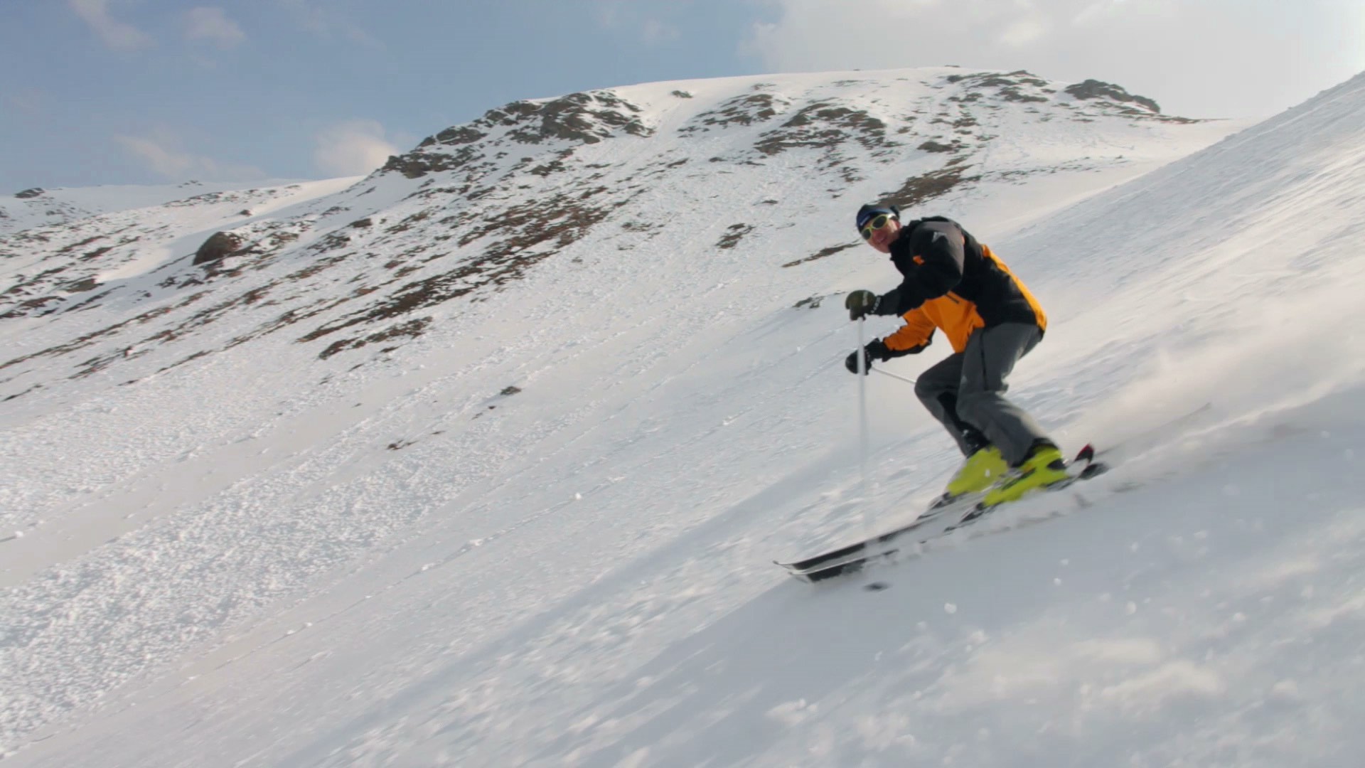 Person skiing down a snowy mountain slope with a rocky peak in the background under a clear sky.