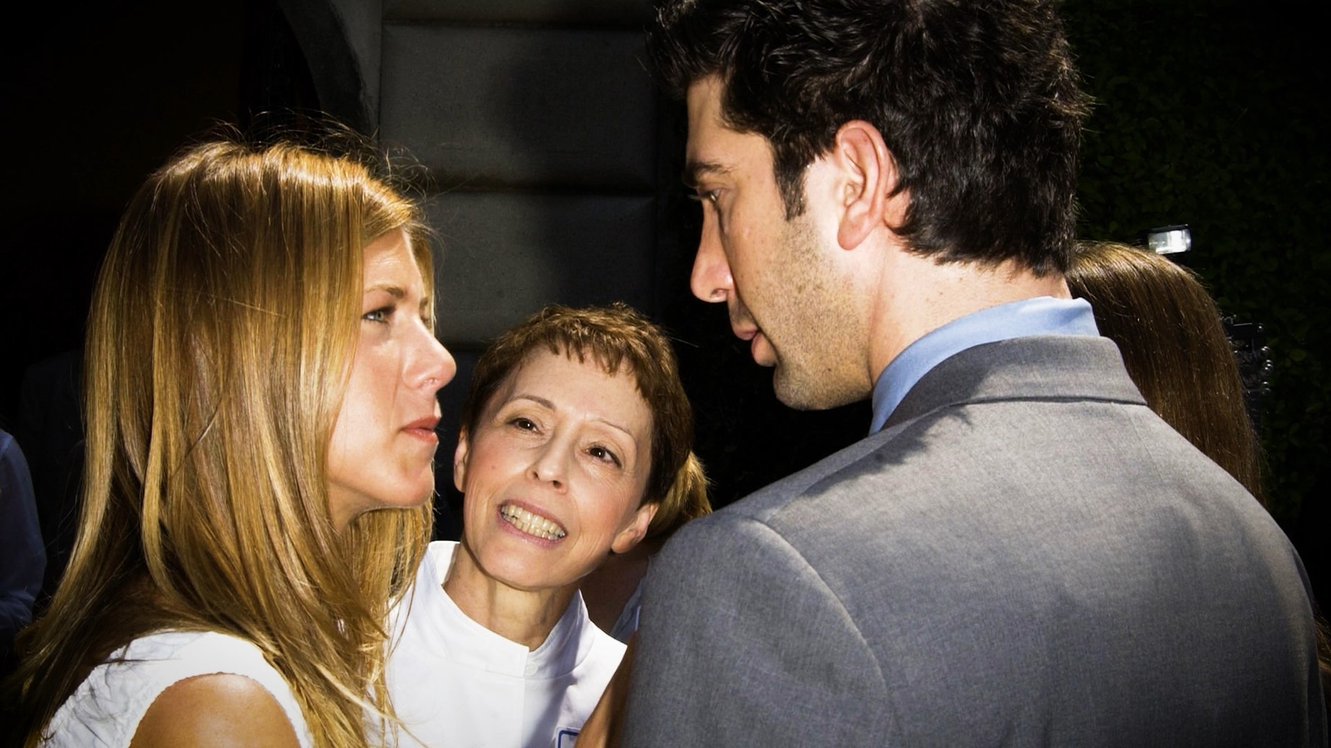 Three people in conversation at an event; one woman smiling at two others.