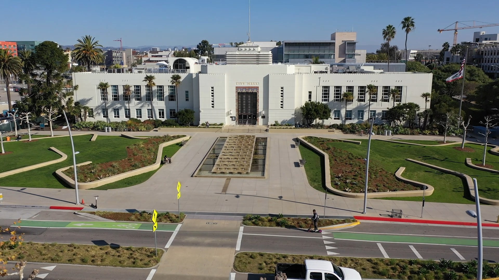 Aerial view of a white city hall building with a garden and fountain in front, surrounded by green lawns.