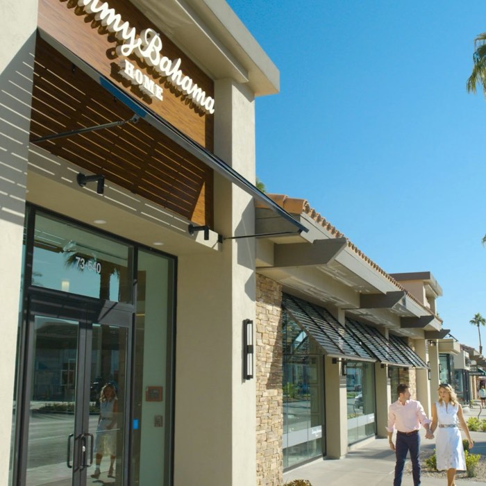 Two people walking past a Tommy Bahama Home store on a sunny day.