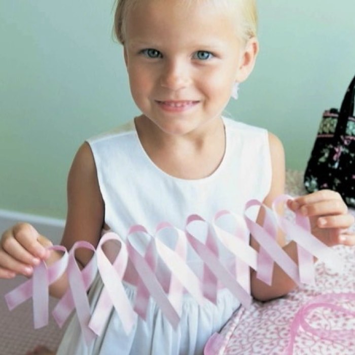 Child in white dress holding multiple pink ribbons, smiling at the camera.